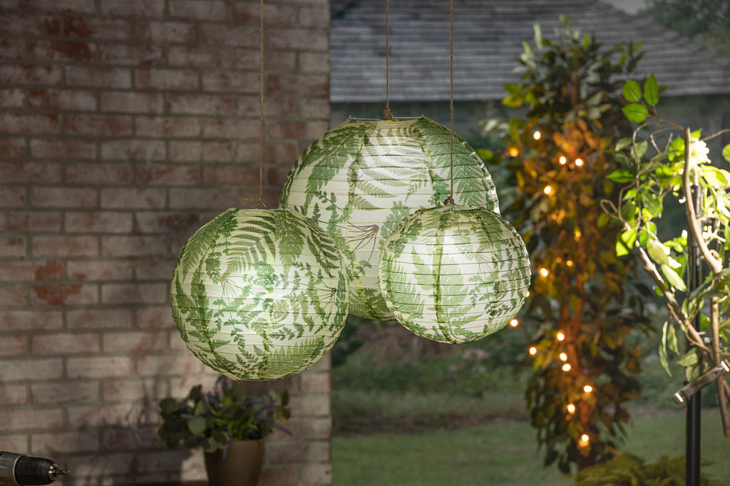 Set of three fern paper lanterns glowing in a porch setting.