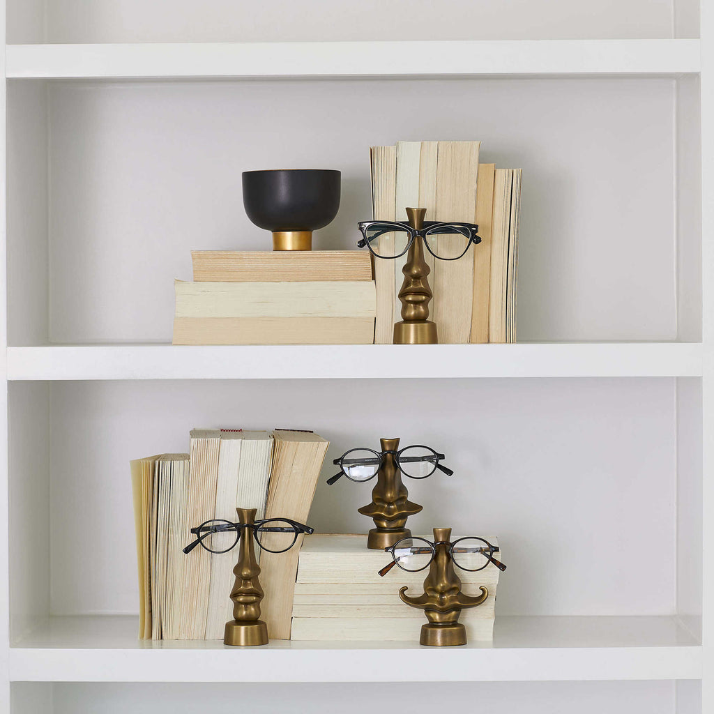 Brass eye-shaped sculpture with an antique finish, designed as a decorative eyeglass holder. Pictured here on a bookshelf.